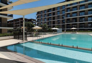 A swimming pool with a clear blue water surface, surrounded by a covered deck area with umbrellas. - Seafront Apt w/ Pool & Gym near Attractions (Sharjah)