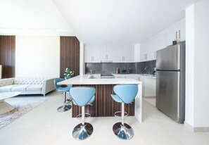 A modern kitchen with white cabinets, a stainless steel refrigerator, and a central island with bar stools. - Seafront Apt w/ Pool & Gym near Attractions (Sharjah)
