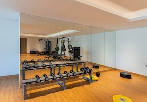 A gym with a mirrored wall, weight racks, and exercise equipment.