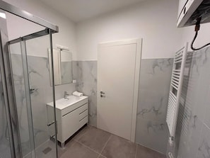 Een badkamer met een douchecabine van glas, een wit wastafelmeubel met een spiegel, en een witte deur.
