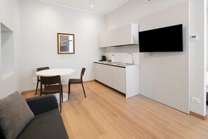 Eine moderne Küche mit Flachbildfernseher, einem Essbereich mit rundem Tisch und Stühlen sowie einer Couch mit Kissen.