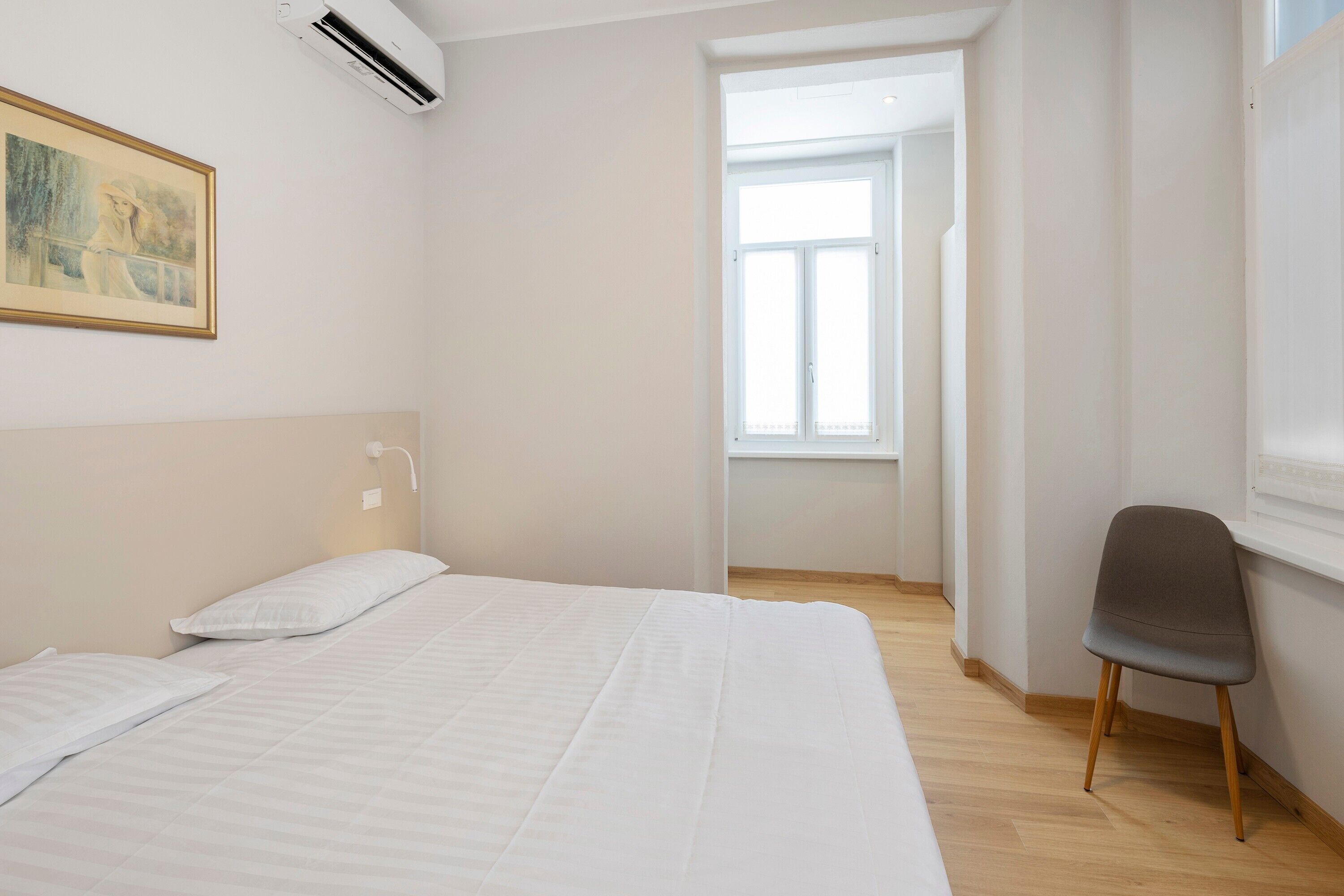 Ein Schlafzimmer mit einem Bett, einem Sessel, einem Gemälde und einem Fenster.