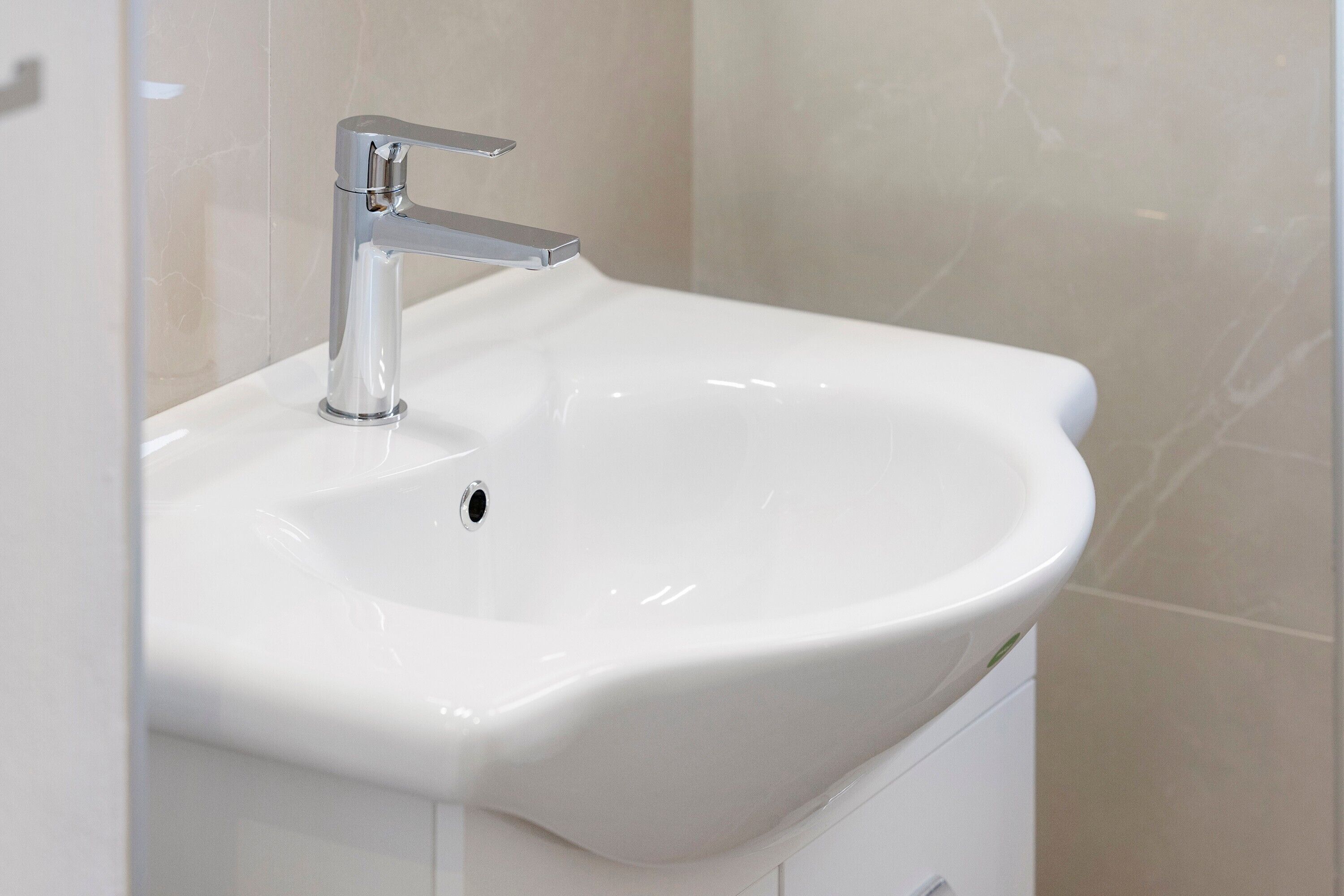 A modern bathroom with a white sink, chrome faucet, and marble tiles.