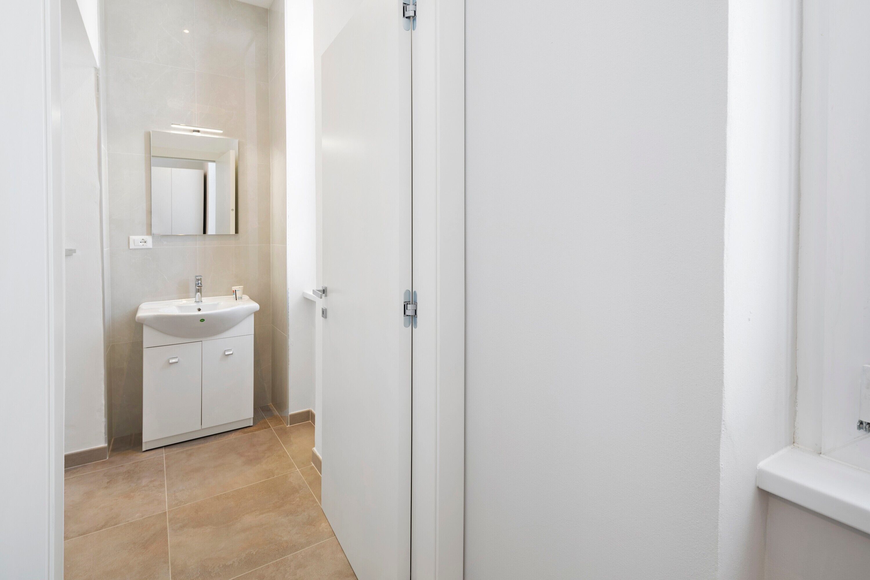 Casa de banho com lavatório branco, espelho e porta.