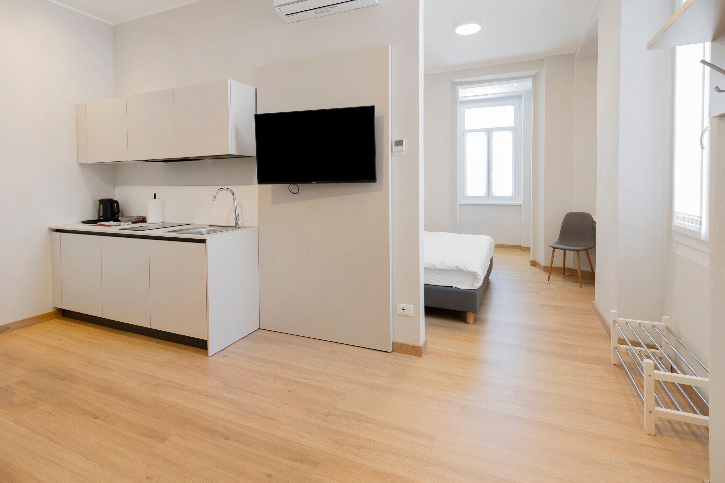 Een kleine kamer met een kitchenette, een bed, een stoel en een radiator.