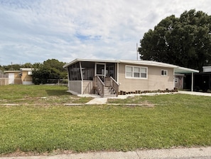 A single-story mobile home with a porch, a small deck, and a front yard.
