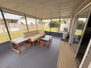 A covered patio with a sofa, table, and chairs, overlooking a backyard with a fence and houses.