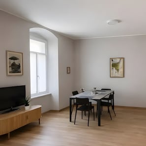Een moderne woonkamer met een flatscreen televisie, een eettafel met stoelen, een raam en twee ingelijste foto's aan de muur.