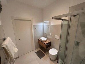 A modern bathroom with a glass shower enclosure, a white toilet, and a wooden vanity with a sink. - Apartment 'Castello' with Wi-Fi (Gorizia)