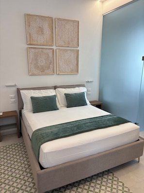 A neatly made bed with a green throw, a bedside table, and a wall with four framed floral patterns.