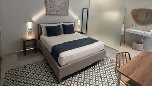 Een moderne slaapkamer met een bed, nachtkastjes, een bedlampje, een wandspiegel, een klein tafeltje en een stoel.