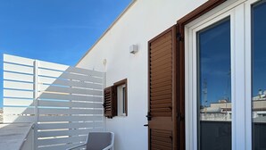 Un balcón con una silla blanca, una puerta de madera y una pared blanca.