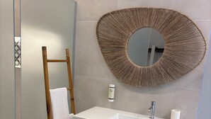 Un baño con una escalera de madera, un lavamanos blanco, un espejo redondo y una cesta tejida.