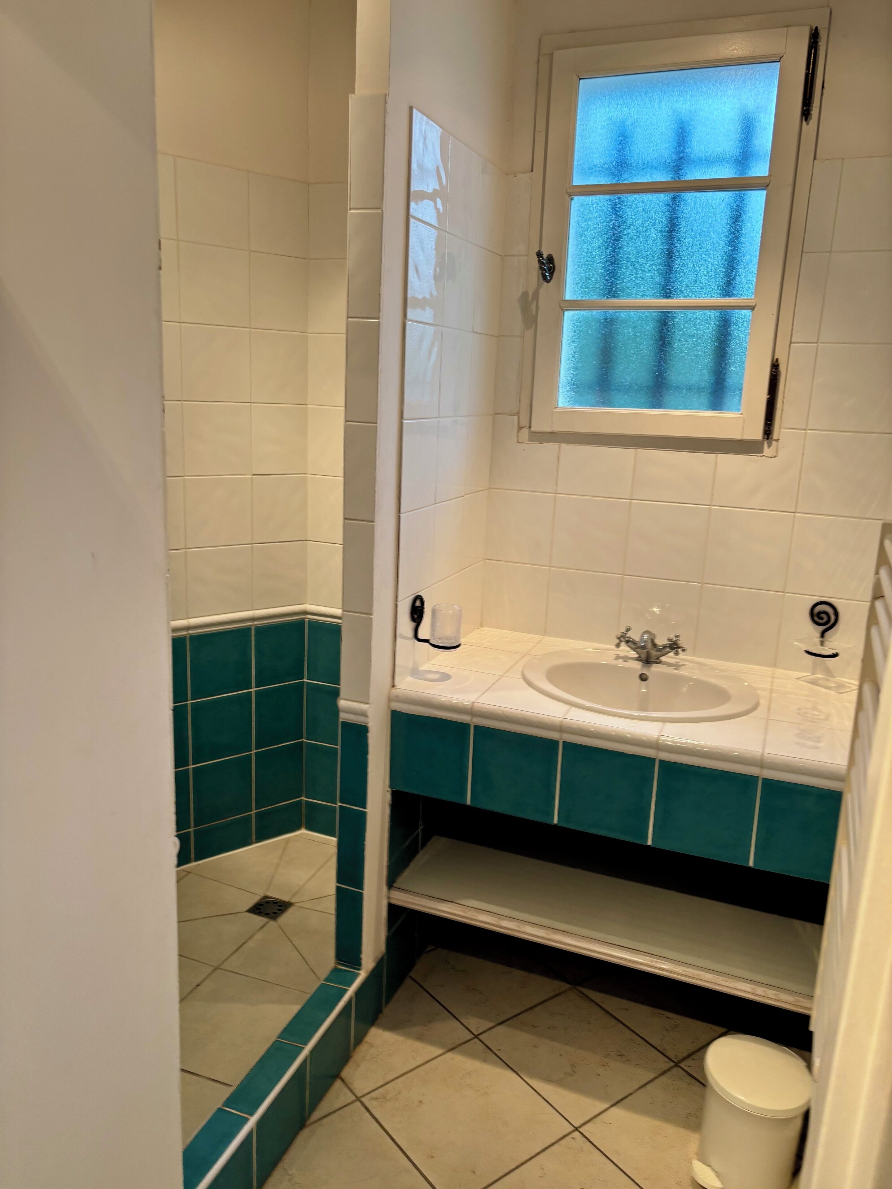 Un baño con azulejos blancos y turquesa, un lavabo, una ventana y un espejo.