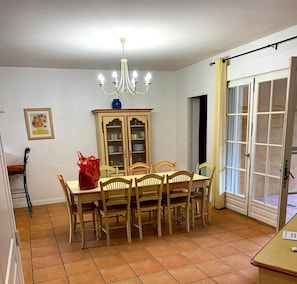 Ein Esszimmer mit Tisch, Stühlen, einer Chandelüster, einem Schrank und einer Glastür.