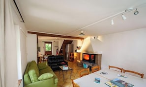 Una sala de estar con un sofá verde, una mesa de comedor con sillas, una chimenea y una cocina al fondo.