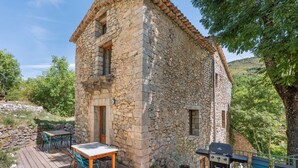 A stone building with a wooden deck, a table, chairs, and a grill.