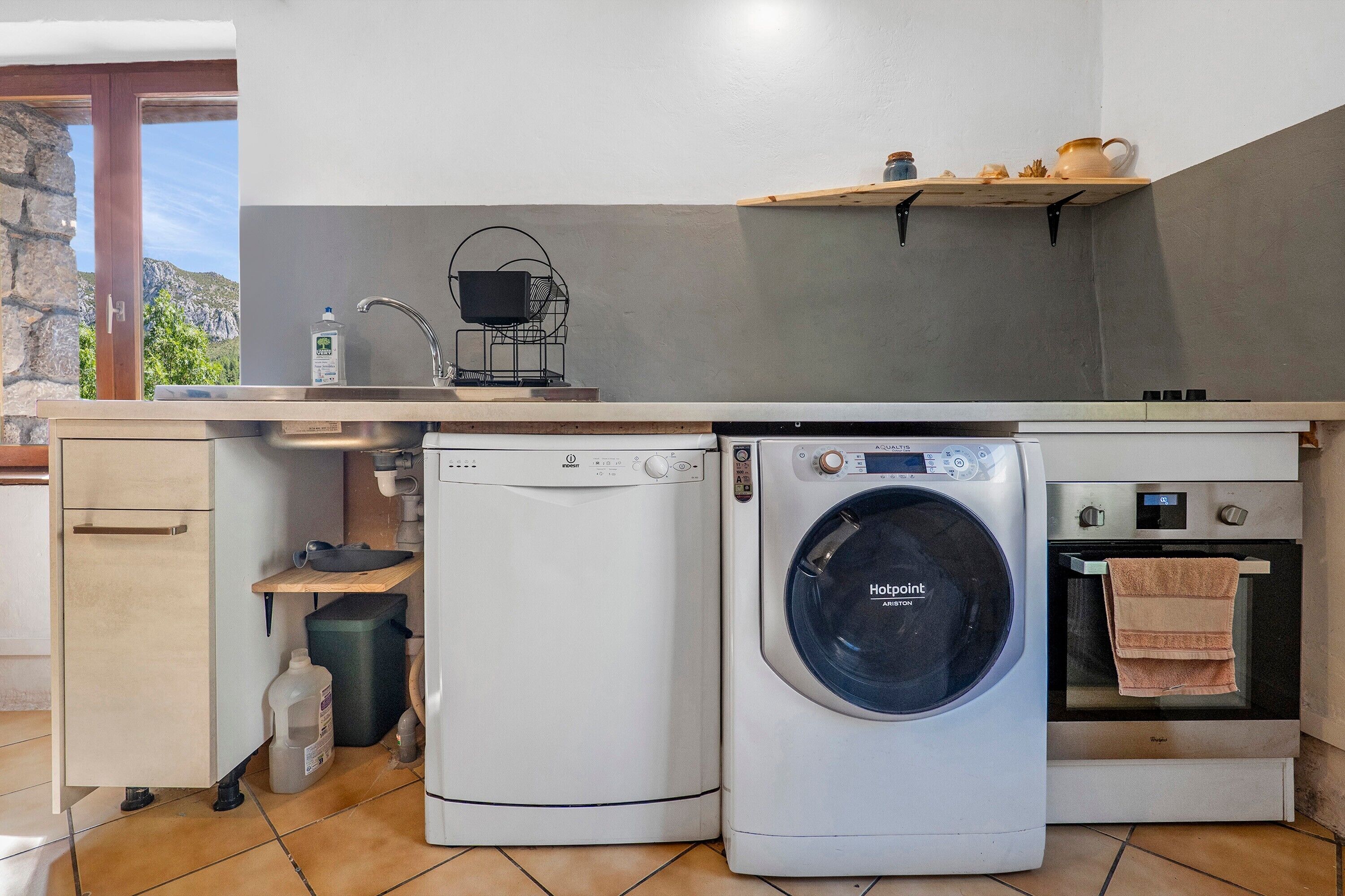Una cucina compatta con lavatrice, piccolo forno e ripiano con stoviglie.