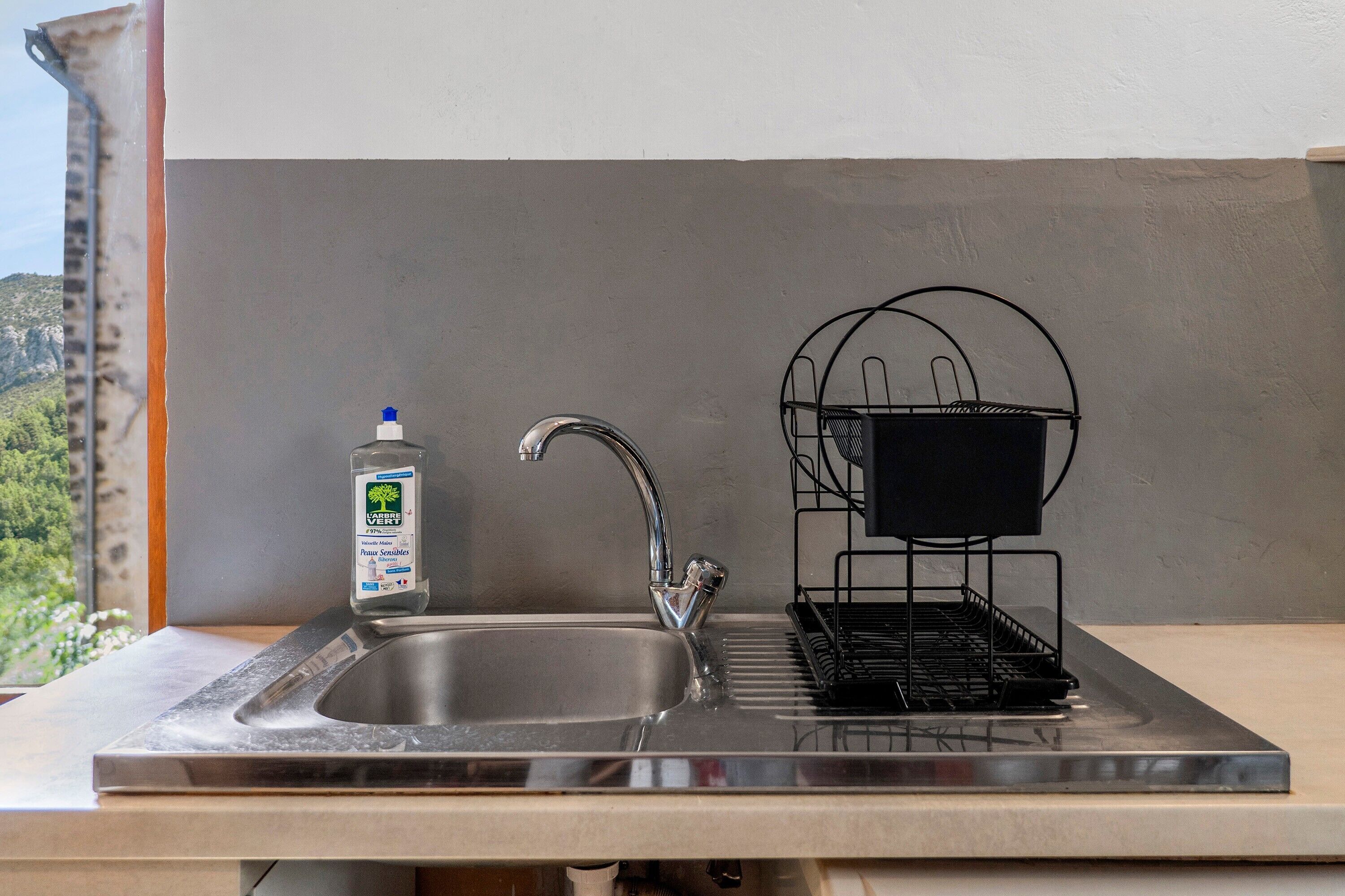 Un évier de cuisine avec un robinet, une bouteille de liquide vaisselle et un égouttoir noir.