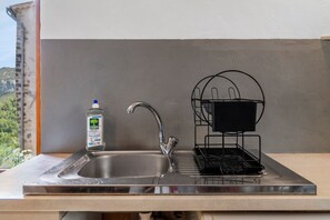 A kitchen sink with a faucet, a bottle of dish soap, and a black dish rack.