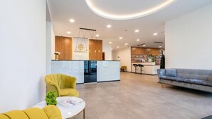 A modern living area with a sofa, a yellow armchair, a round table, and a kitchen in the background.