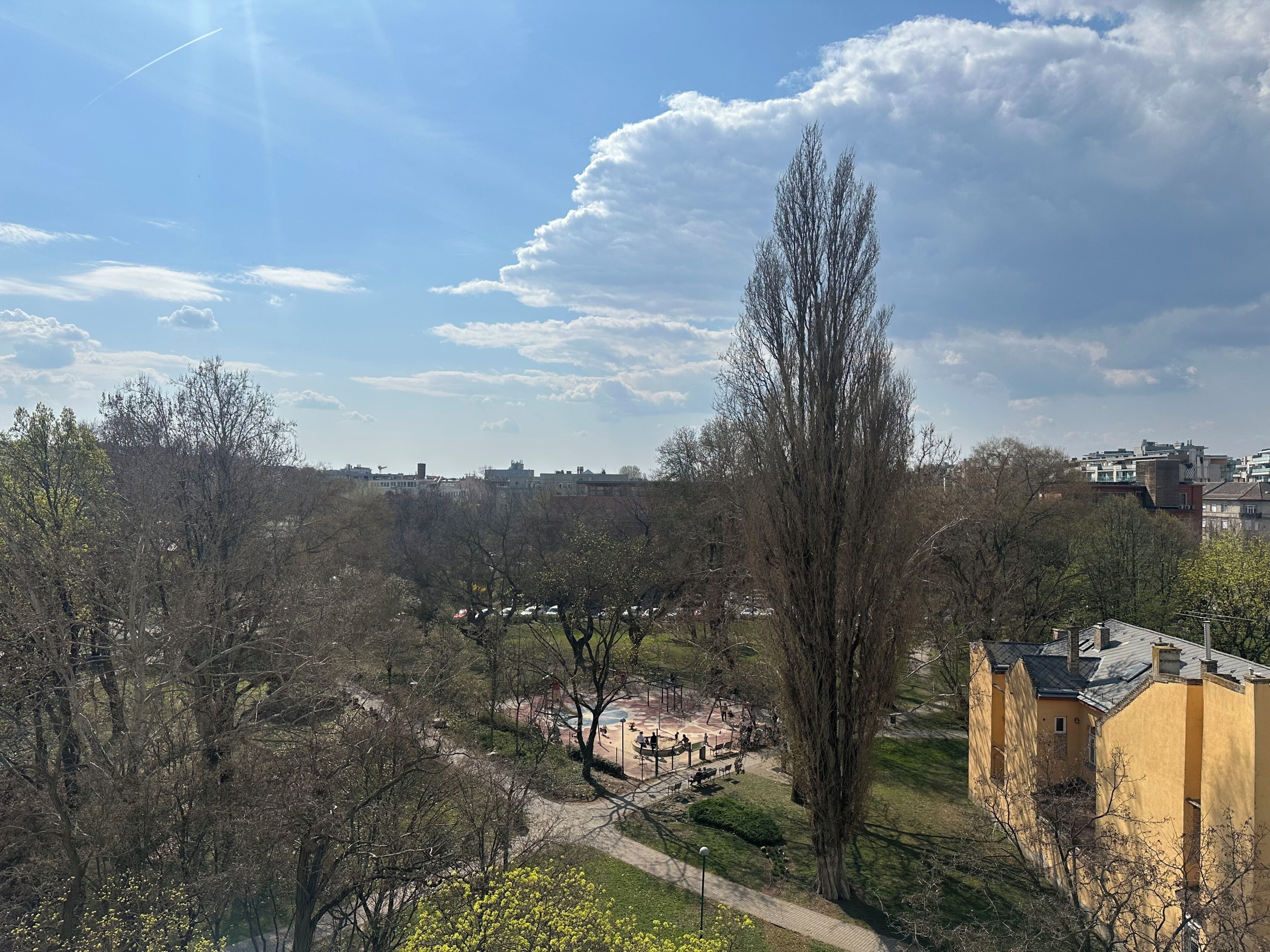 Un parc avec une aire de jeux, un bâtiment jaune et un grand arbre.