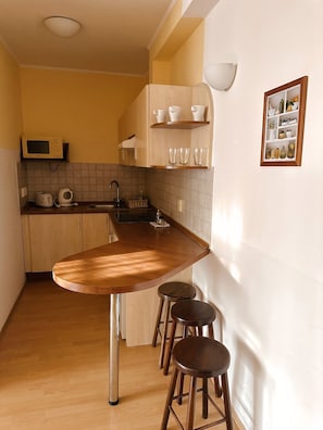 A compact kitchen with a wooden bar counter, stools, a microwave, and a sink. - OB44 Apartments Budapest (Budapest)