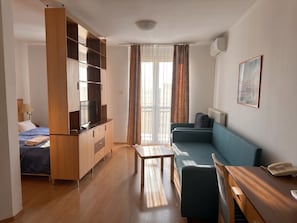 A compact hotel room with a bed, a TV, a sofa, a small table, and a phone on a desk. - OB44 Apartments Budapest (Budapest)