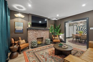 A modern living room with a brick fireplace, leather sofas, a flat-screen TV, and a dining area with a patterned rug. - Welcome to Sue Zen Urban Retreat — Grandview Heights, Columbus (Grandview Heights)