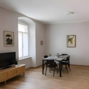 A modern living room with a flat-screen TV, a dining table with chairs, a wooden cabinet, and a large window. - Apartment 'Corso' with Wi-Fi (Gorizia)