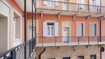 Un immeuble à plusieurs étages, doté de balcons, de volets blancs et d’une façade beige.