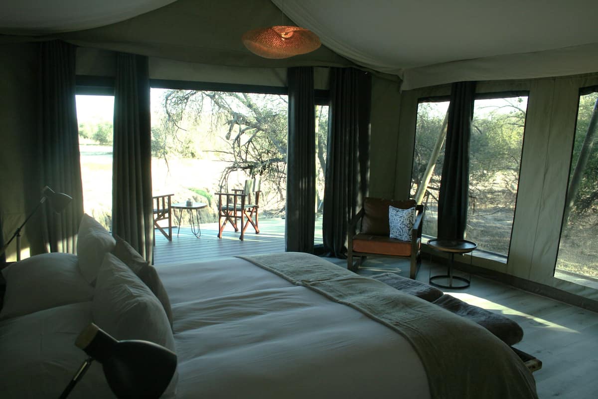 A bedroom with a large bed, a chair, a table, and a view of the outdoors.