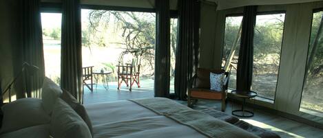 A bedroom with a large bed, a chair, a table, and a view of the outdoors.