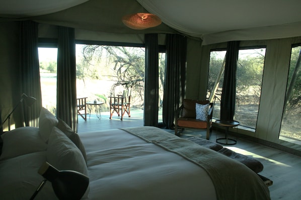 Une chambre avec un grand lit, une chaise, une table et une vue sur l’extérieur.
