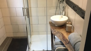 Ett badrum med en duschavdelning med glasväggar, en vit handfat, en handdukshängare och en liten spegel.