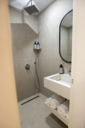 Een badkamer met een douche, wastafel en spiegel.