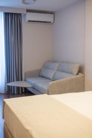 Een hotelkamer met een bank, een klein tafeltje, een airconditioning en een bed.