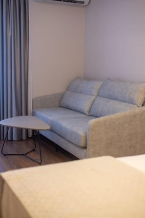 A room with a grey sofa, a small table, and a curtain. - Voko by Uka Boutique Hotel (Tiranë)