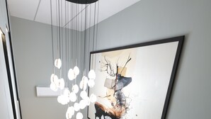 Un interior moderno con una escalera de madera, una lámpara colgante y un cuadro abstracto grande en la pared.