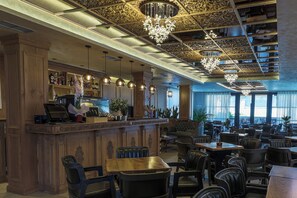 A bar area with wooden paneling, a counter with a computer, and a chandelier. There are multiple tables and chairs arranged for dining. - Voko by Uka Boutique Hotel (Tirana)