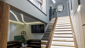Un interior moderno con una escalera, un sofá de cuero, una mesa de centro de madera y un reloj en la pared.