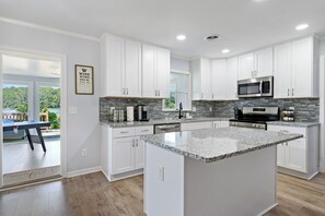 Una cocina moderna con armarios blancos, encimeras de granito y electrodomésticos de acero inoxidable.