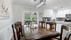 Un espace repas avec une table et des chaises en bois, un lustre et une vue sur l’extérieur.