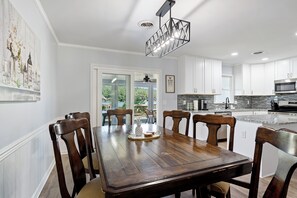 Un comedor con mesa y sillas de madera, una araña y vistas al exterior.