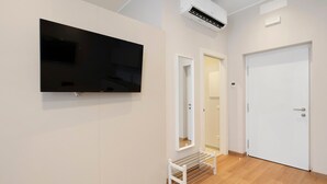 Een hal met een flatscreen televisie aan de muur, een witte deur en een bank.