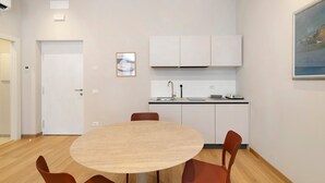 Een moderne keuken met witte kasten, een ronde tafel met stoelen en een schilderij aan de muur.