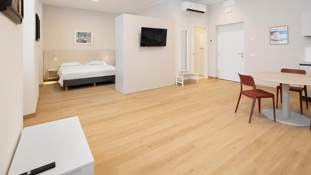 Een moderne hotelkamer met een bed, een televisie, een zithoek met stoelen en een kleine tafel.