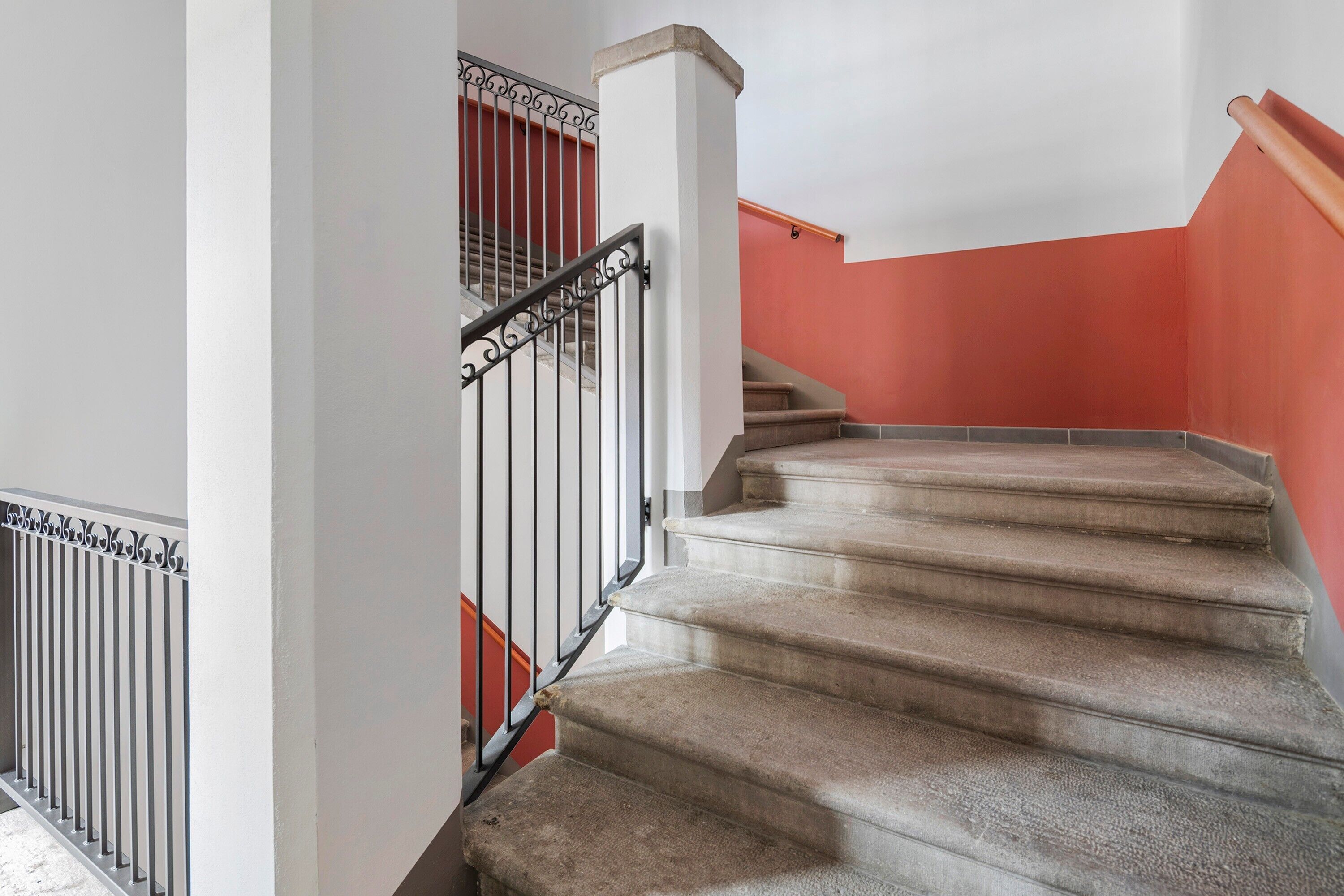A staircase with a handrail and a metal railing, leading to a landing with a red wall.