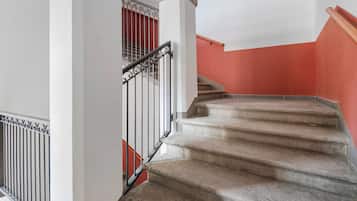 A staircase with a handrail and a metal railing, leading to a landing with a red wall.