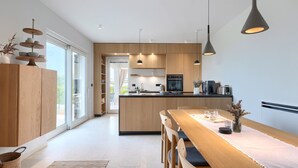 Una cocina moderna con armarios de madera, una isla central, luces colgantes y vistas a través de la puerta de vidrio.